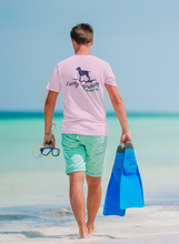 Load image into Gallery viewer, Person walking on a beach with snorkeling gear, wearing a pink t-shirt with a Lucky Labrador Logo and green shorts.