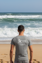 Load image into Gallery viewer, Person wearing a gray t-shirt with 'Lucky Labrador Surf Co' logo on the back at the beach