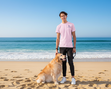 Load image into Gallery viewer, Person in pink shirt with Lucky Labrador  logo and a dog on a beach background